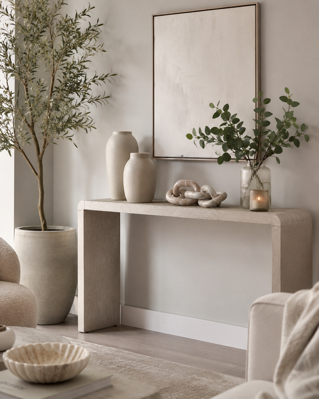 Living room decorative accessories on a console table with ceramic vases, faux olive tree, eucalyptus stems, candle and sculptural chain decor