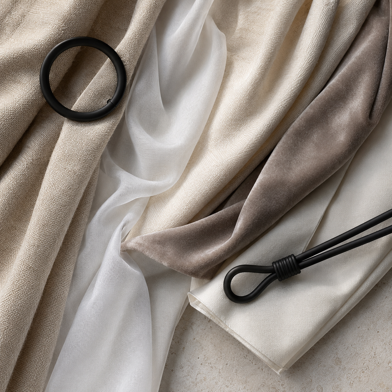 Close-up of layered curtain fabrics with black curtain ring and tieback on a neutral stone surface.