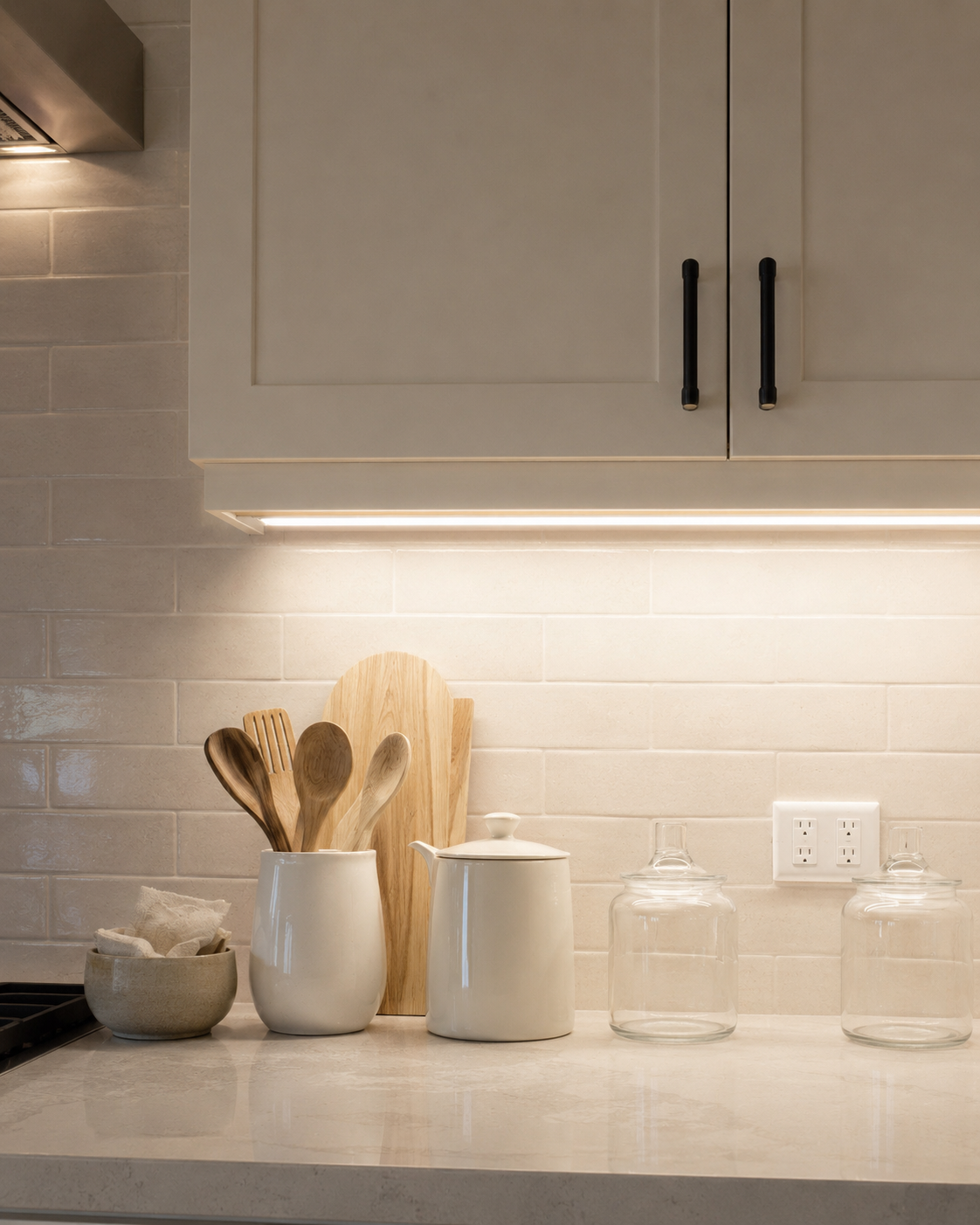 Under cabinet task lighting above a clean kitchen counter with ivory cabinets and soft neutral styling