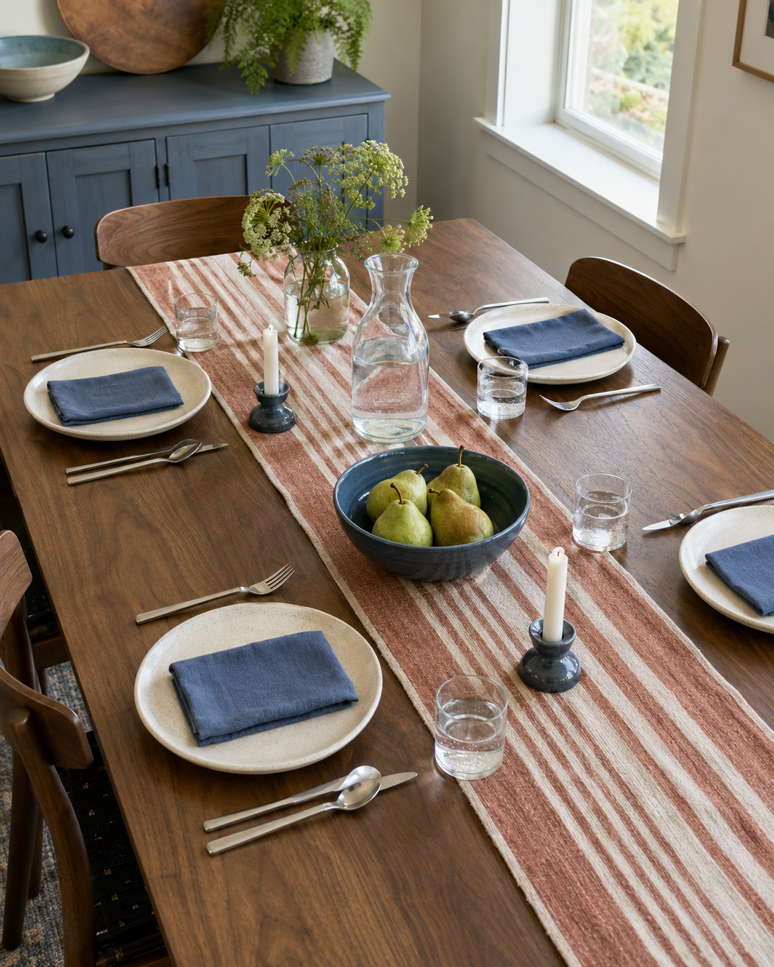 Walnut dining table styled with a striped runner, blue napkins, ceramic plates, pears and candle holders