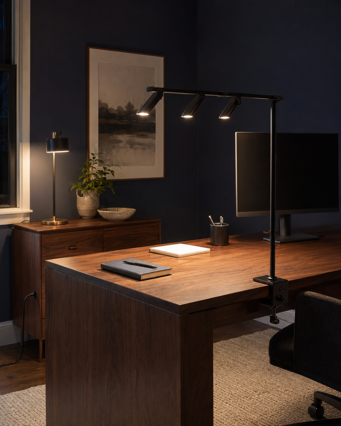 Walnut home office at evening with a three-head clamp lamp and brass-accent table lamp creating focused light.