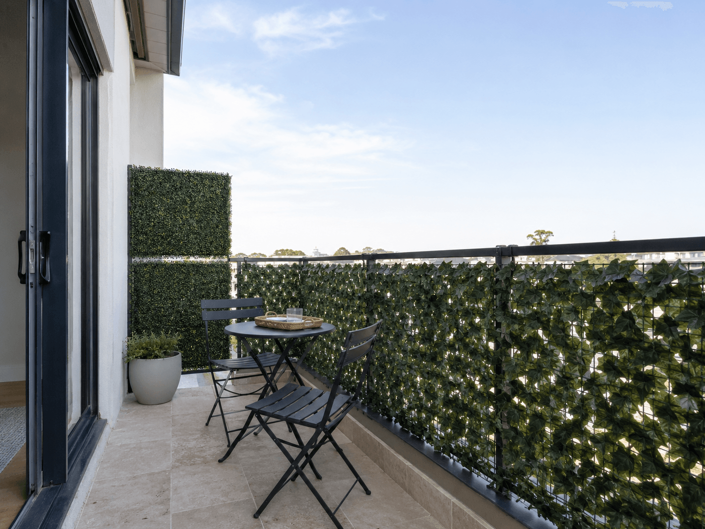 Narrow apartment balcony with green screening along the exposed edges and a compact dark bistro set.