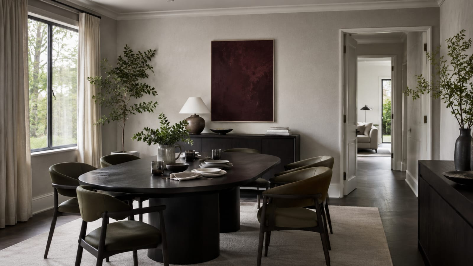 Dark oval dining table with six upholstered chairs, sideboard and a clear walkway into the adjoining room.