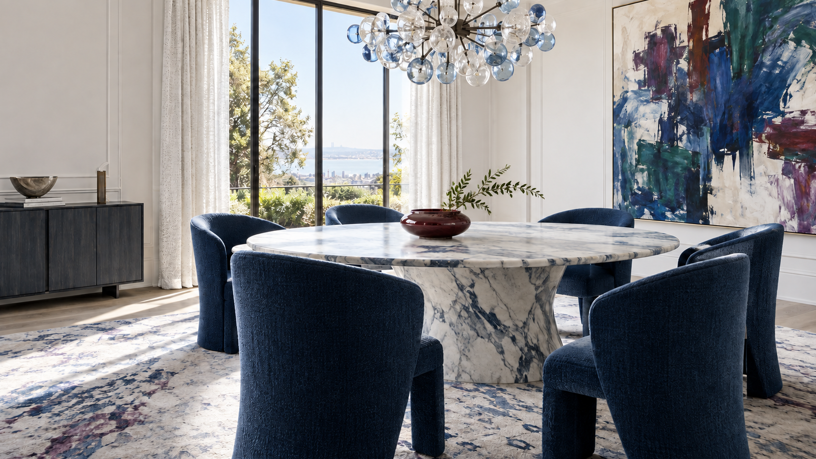 Bright contemporary dining room with sapphire chairs, sculptural stone table, colorful abstract art and glass chandelier.