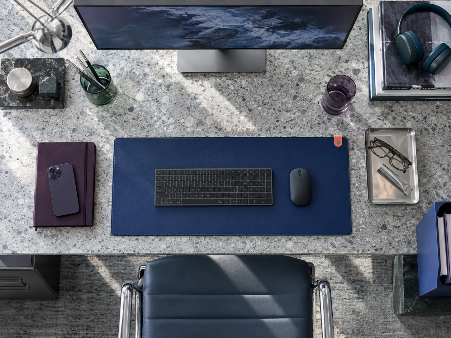 Overhead home-office desk showing chair position, active work surface, monitor, headphones and supporting tools.