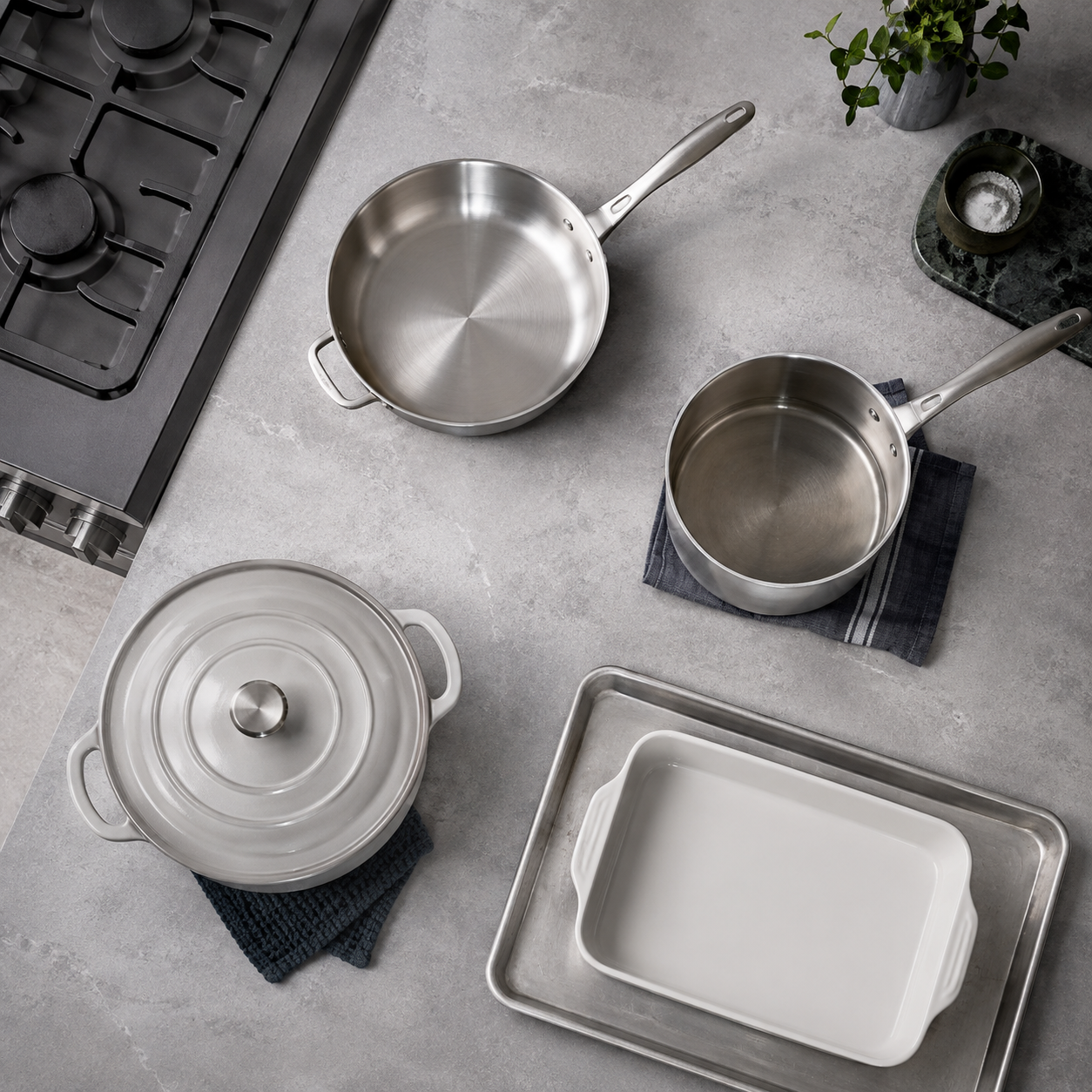 Kitchen Cookware & Bakeware Essentials - Ravnora Decor Top-down arrangement of a skillet, saucepan, deeper enameled cookware and bakeware illustrating different cooking jobs.