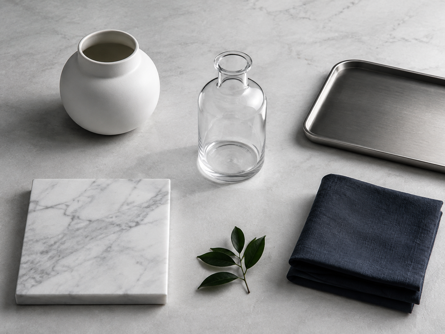 Kitchen Counter Decor - Ravnora Decor Cool-toned material board combining white ceramic, clear glass, brushed metal, pale stone, navy textile and green foliage.